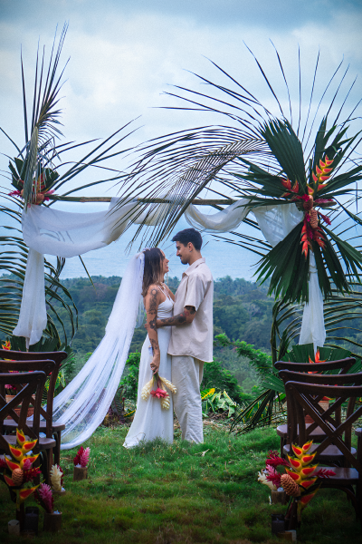 Bride and groom embracing beneath a tropical wedding arch during an outdoor destination wedding ceremony at Promised Land Tayrona, Colombia.